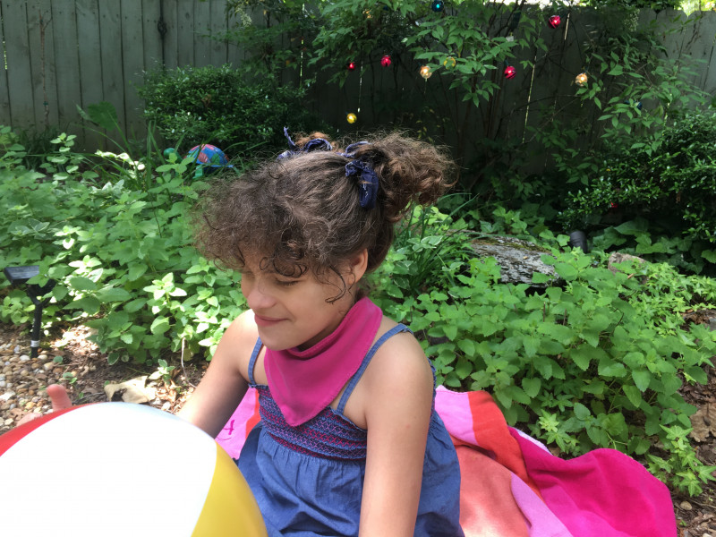 DIY projects and special needs products | Angelman Syndrome News | With her hair in a ponytail, Juliana, 11, wears a bandana bib her mom made as she plays outdoors with a beach ball