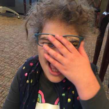 living with angelman syndrome | Angelman Syndrome News | Juliana tries on a new pair of blue glasses and smiles