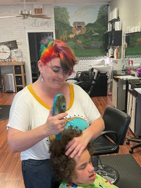 getting a haircut | Angelman Syndrome News | photo showing a stylist with multicolored hair using a brush on Juliana's hair