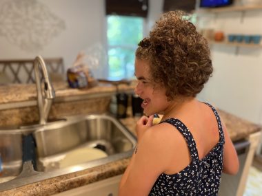 lifelong medical care | Angelman Syndrome News | Juliana smiles in the kitchen after putting her dirty dishes in the sink — one of the daily living skills she's working on.